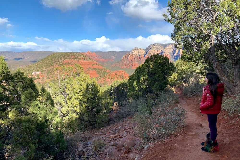 A child in a red jacket and fuzzy boots overlooking the gorgeous, tree-filled view from the Airport Mesa Overlook in Sedona. 