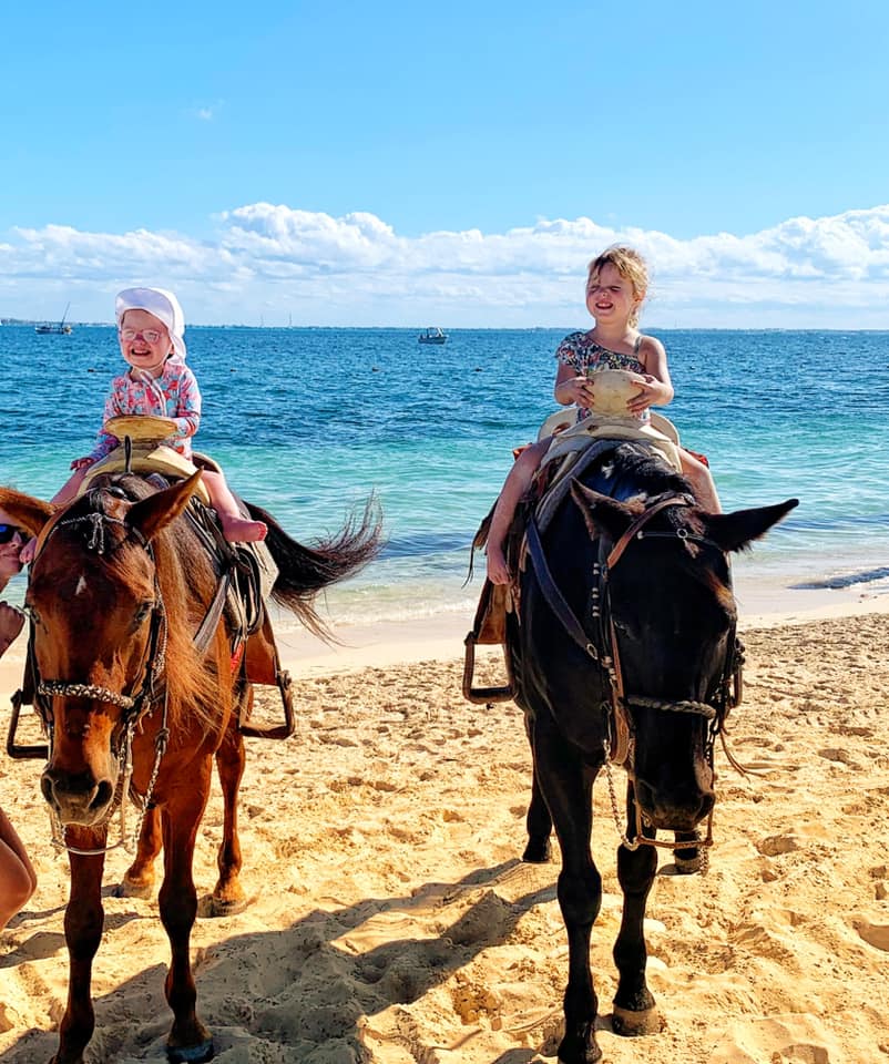 Two kids sit atop horses on the beach in Cancun.