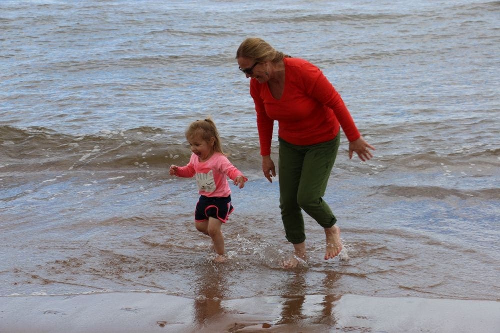A young girl and her grandma laugh as they run through waves on a beach in Prince Edward Island. Shared joy is a major benefit of multigenerational travel.