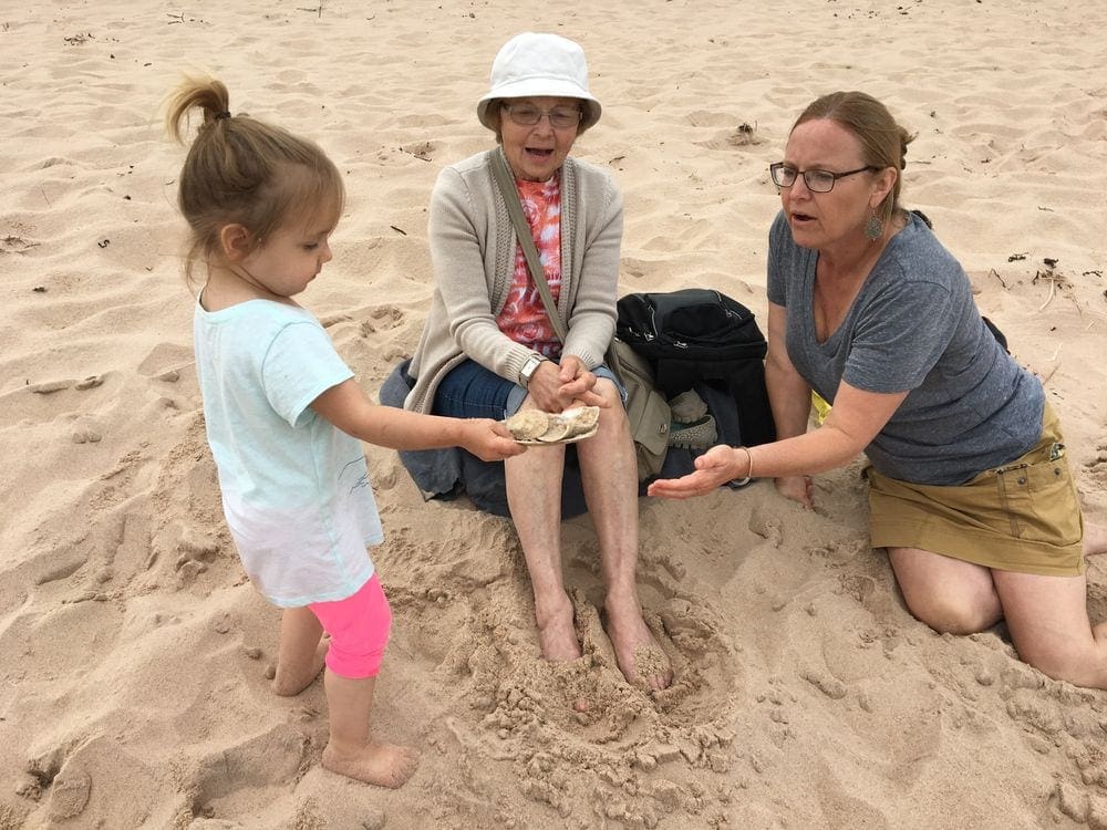 A young girl holds out shells on a beach in Prince Edward Island as her grandmother and great-grandmother look on with interest and delight. Seeing the world through a new lens is one of the best reasons for multigenerational travel.