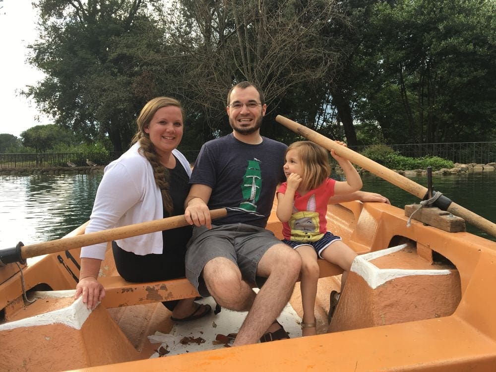 A family of three sits smiling in a paddle boat on the pond in the Borghese Villa in Rome, Italy.