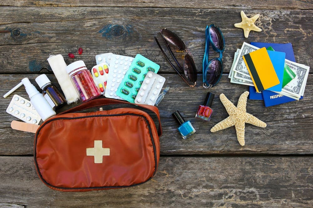 A first aid kit sits on the bottom left with many essential travel first aid kit supplies for kids coming out of the bag onto the table, including several types of medication.
