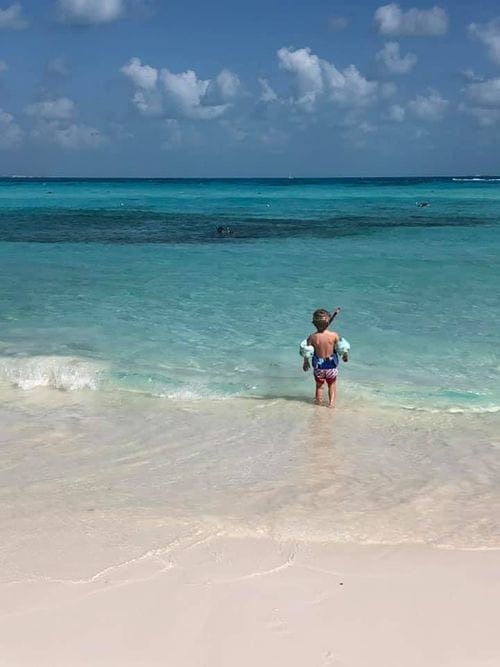 A young boy wearing arm floaties and a snorkle walks into crystal blue water on a Cancun beach.