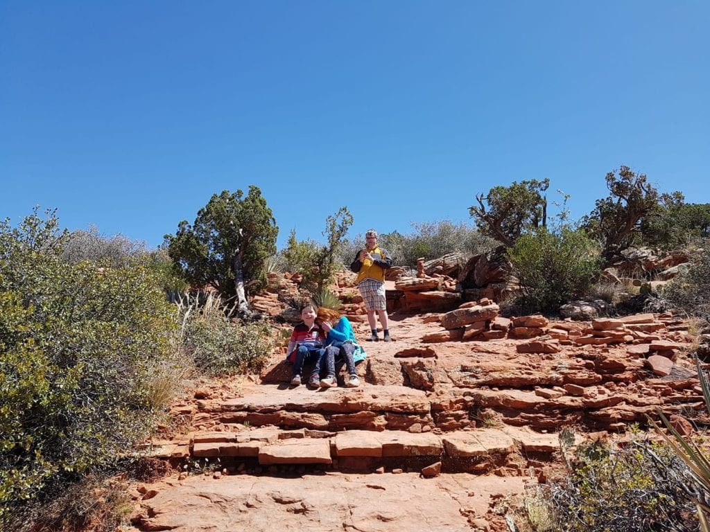Two kids sit amongst red rocks while a third stands in the background.