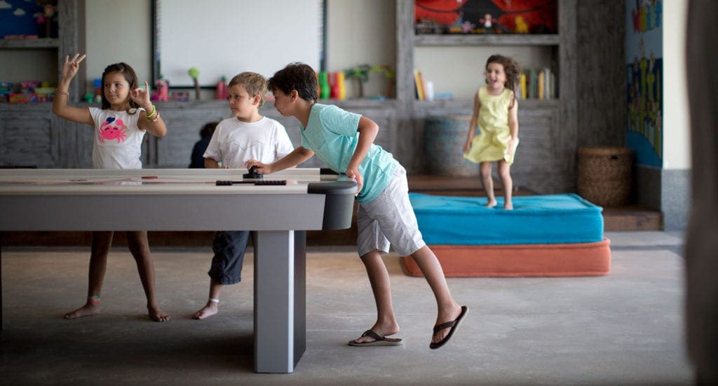 One young boy plays air hockey at the Kids Club at the NIZUC Resort and Spa, one of the best family resorts Cancun, while three others cheer him on. A great kids spaces makes this one of the best family resorts in Cancun.