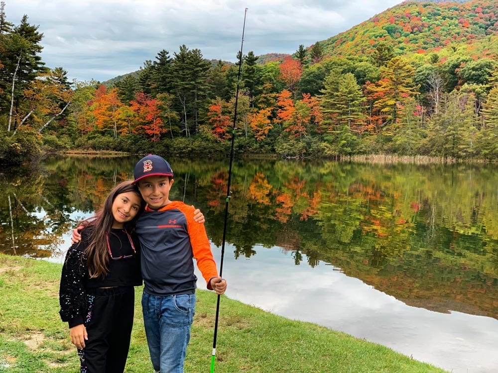 Sister and brother stand close together, while the boy holds a fishing pole on a family vacation.