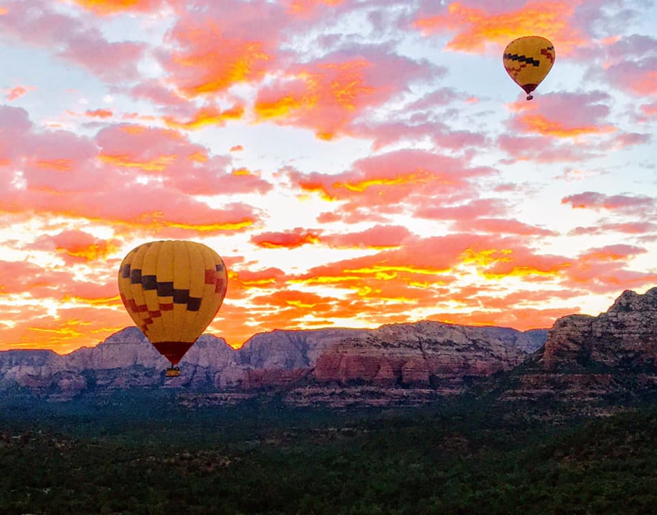 A hot air balloon rising above a beautiful, orange and pink sunset. 