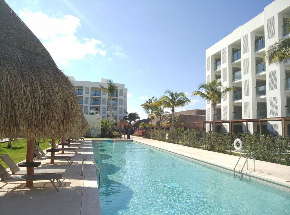 A view of a pristine pool at Finest Playa Mujeres in Cancun, flanked by cabanas on one side and the hotel building on the other.