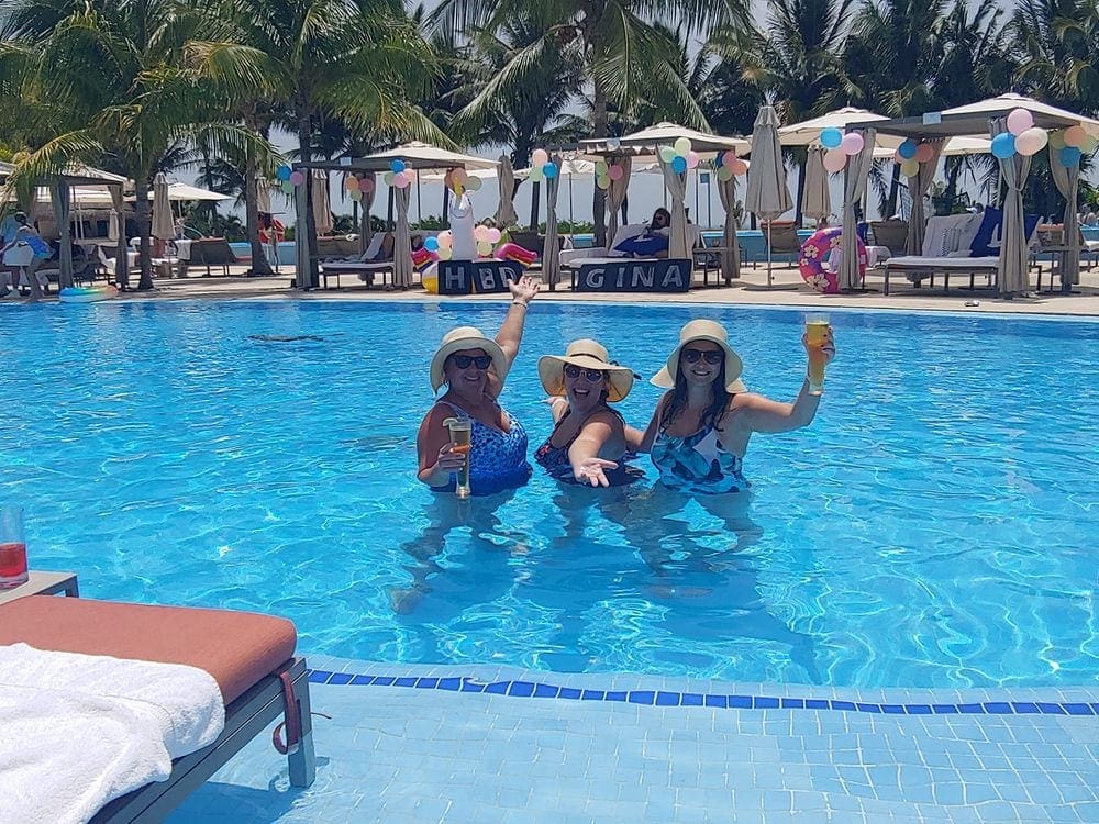 Three women stand smiling with drinks in their hand in a pool at the Grand at Moon Palace Hotel, one of the best family resorts Cancun.