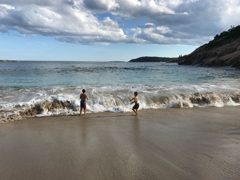 Two young boys run through playful waves on the Atlantic Ocean in Maine.