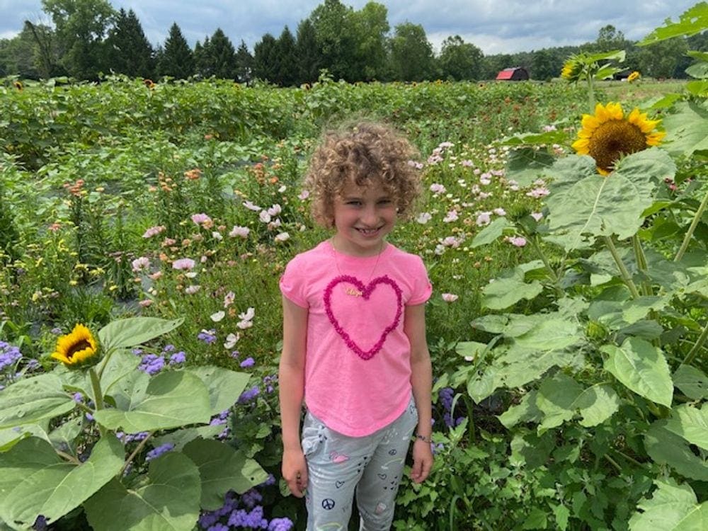 A young girl stands smiling amongst wildflowers and sunflowers at Saunderskill Farm.