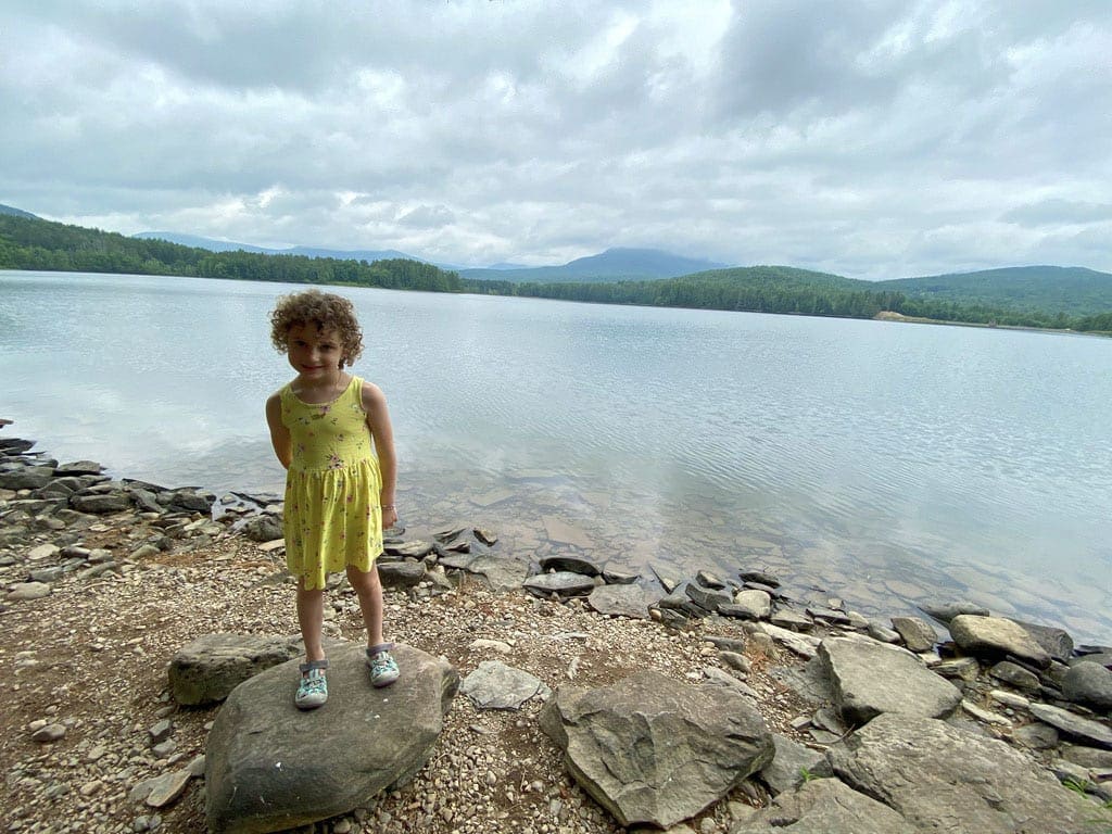 A young girl in a yellow dress stands proudly in front of Cooper Lake.