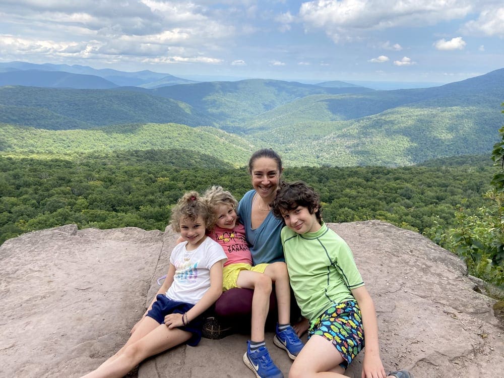 A mom and her three kids sit on a rock overlooking the Catskills, one of the best Labor Day Weekend getaways near NYC with kids.