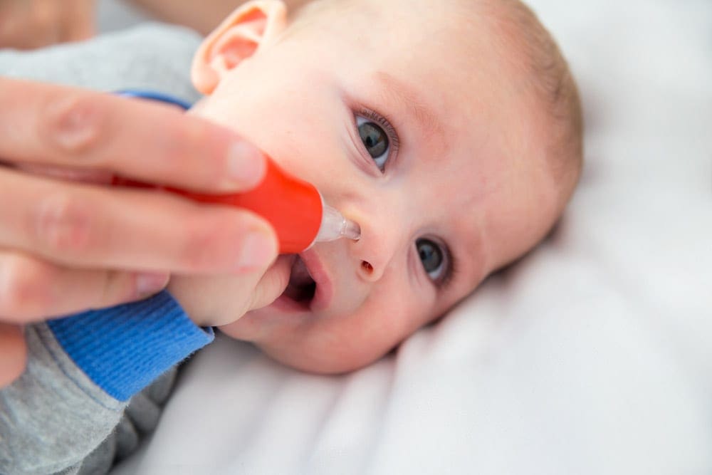 An adult hand uses a suction tool to alleviate the stuffed nose of an infant.