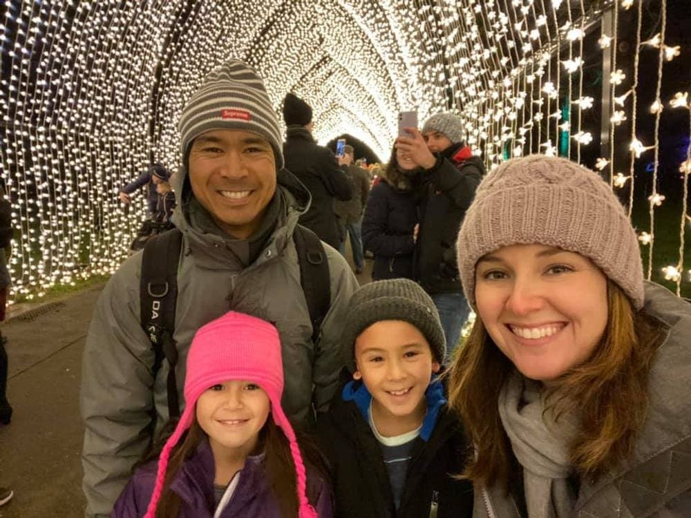 A family of four smiles broadly while walking through a lit up tunnel as part of the Christmas display in the Kew Gardens of London.