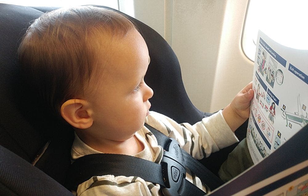 An infant looks at the in-flight safety manual while sitting in her car seat when traveling on an airplane.