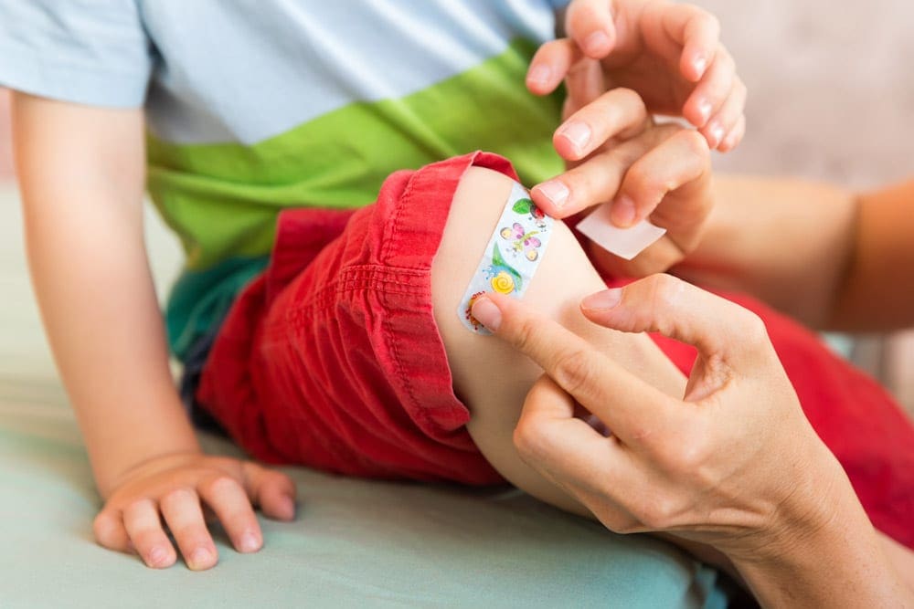 Two adult hands are shown putting a colorful bandange onto a small child's knee.