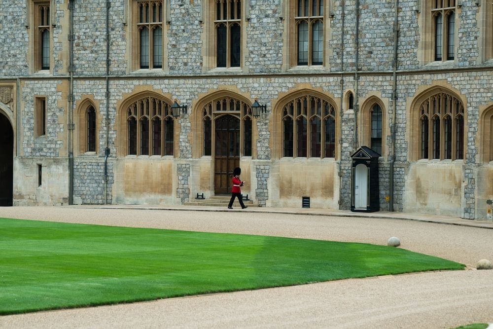 A lone British guard in traditional red uniform walks across the grounds of Windsor Castle.