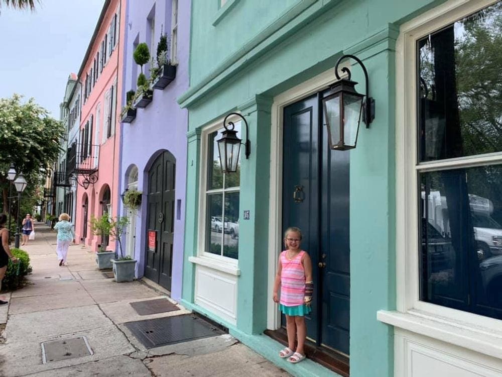 A young girl wearing a colorful shirt standing in front of a street lined with colorful buildings in Charleton, one of the best Thanksgiving destinations in the United States for families.