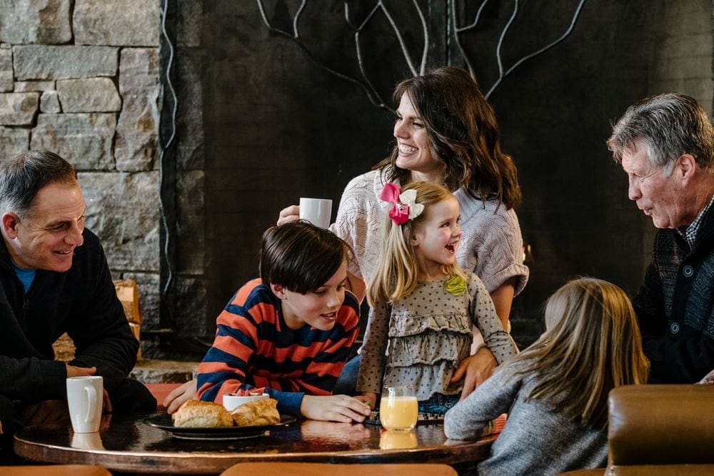 A grandfather, two parents, and three kids enjoy a wonderful morning breakfast at The Lodge at Spruce Peak.