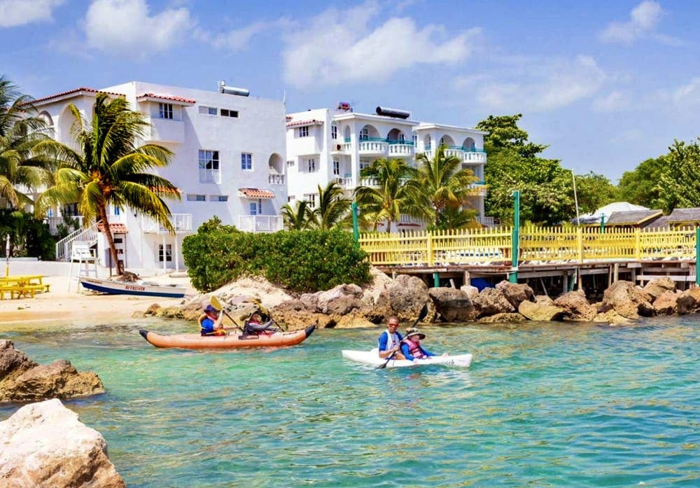 A view of Franklyn D Resort & Spa from the water, featuring two kayaks in the crystal blue water, one of the best Caribbean resorts with baby clubs.