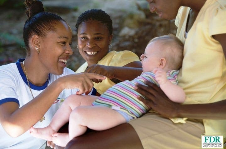 Three baby club staff lovingly hold and pay attention to a baby at Franklyn D Resort & Spa, one of the best Caribbean resorts with baby clubs..