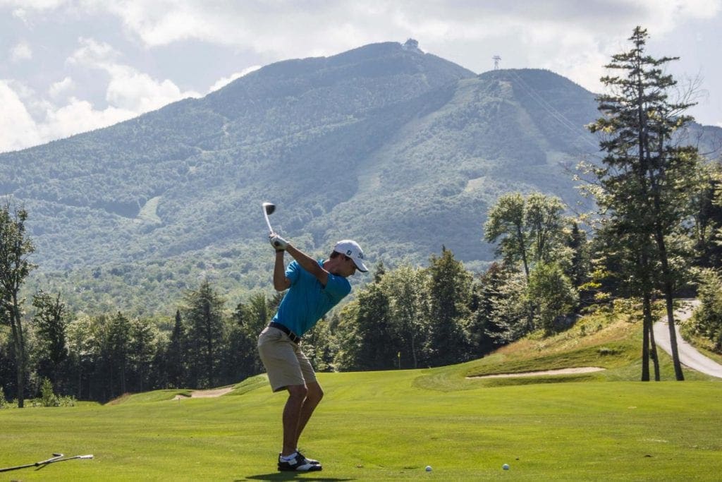 A man takes a large golf swing on a perfect day.