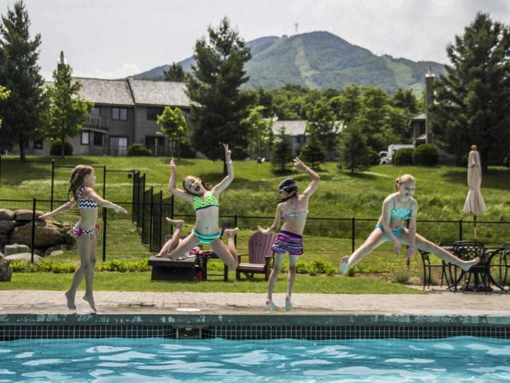 Four kids take huge jumps into the outdoor pool at Jay Peak Resort, one of the best Vermont hotels for families.