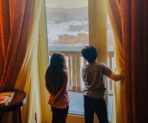 Two children look out a large hotel windown onto the property of the Lodge at Spruce Peak.