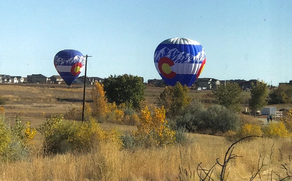 Two Colorado-inspired hot air balloons land in a filed on an autumn day in Colorado. A fall festival is one of the best fall activities in Colorado with kids.