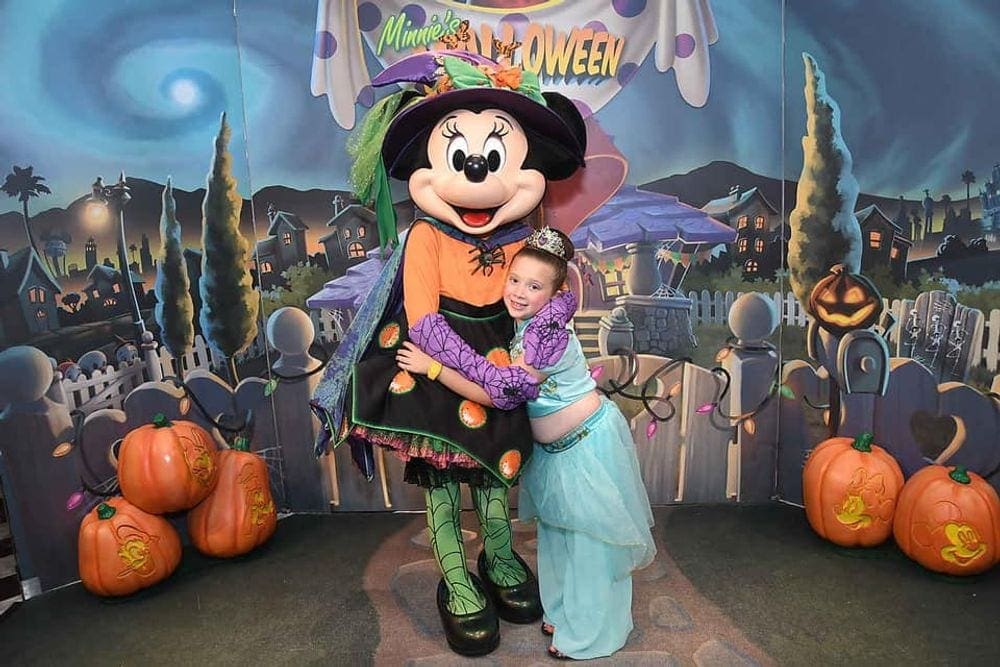 A young girl wearing a Jasmine costume hugs Minnie Mouse in her Halloween outfit.