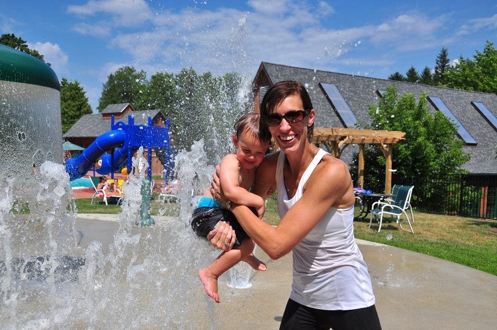 A father holds his baby while enjoying a splash pad at The Tyler Place Family Resort, one of the best all-inclusive hotels in the United States for families.