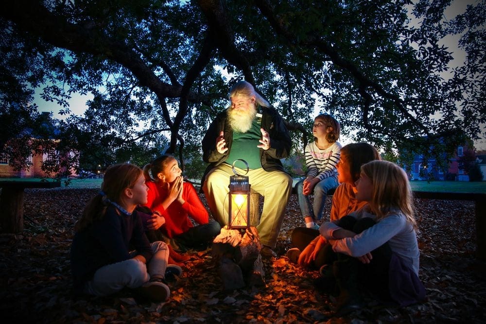 An older gentleman sits telling five kids a ghost story as part of a program at Colonial Williamsburg, one of the best places to go for Halloween.
