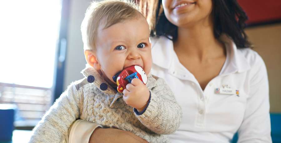 A baby club staff member holds a small baby who is sucking on a toy.