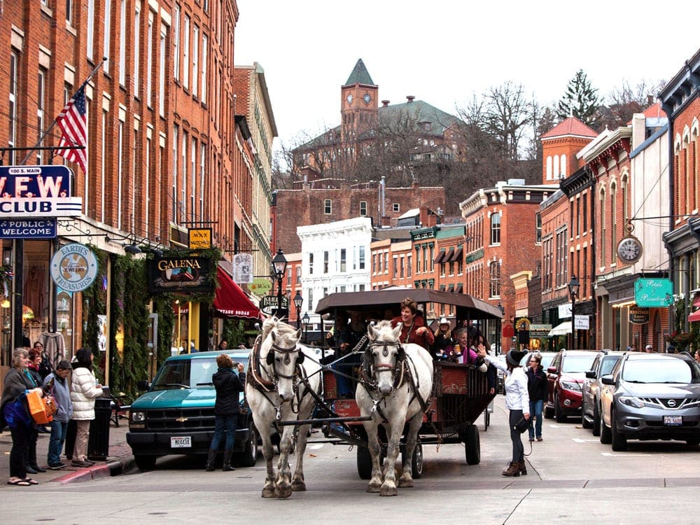 A buggie is pulled by two white horses down the main street of historic Galena, IL, a great stop for a Midwest road trip with kids.