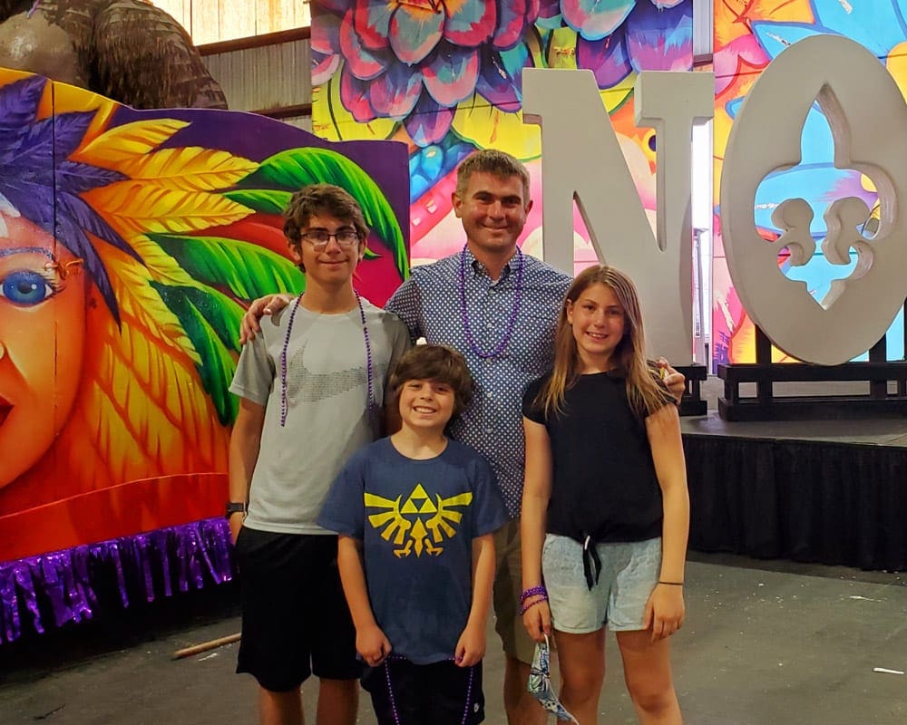 Three kids stand smiling with their dad at Mardi Gras World.