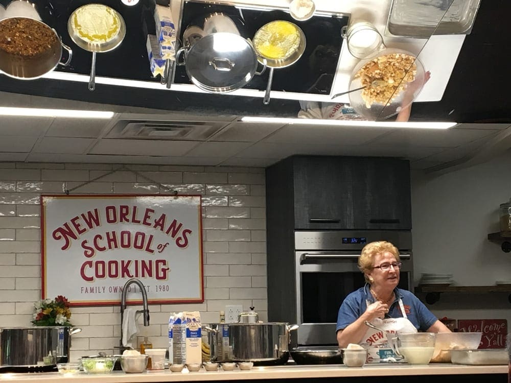 A chef at the New Orleans School of Cooking smiles while she shares a story amidst a cooking lesson.