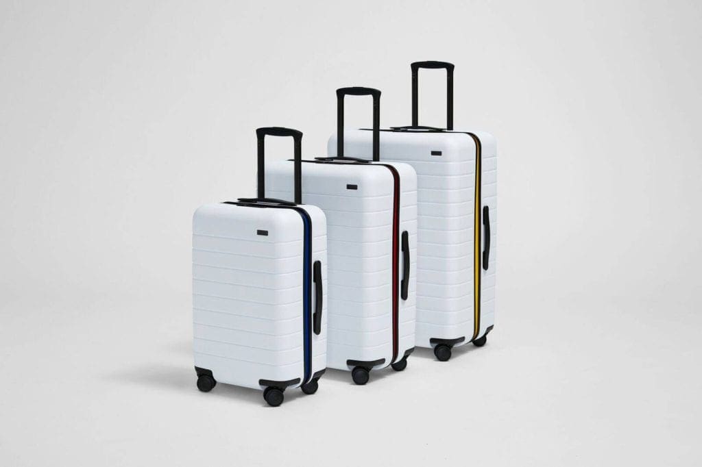 three hard-side white carry-on luggages from Away Bigger with a pop of red, yellow, and black. Away Bigger offers some of the best travel luggage for kids. 