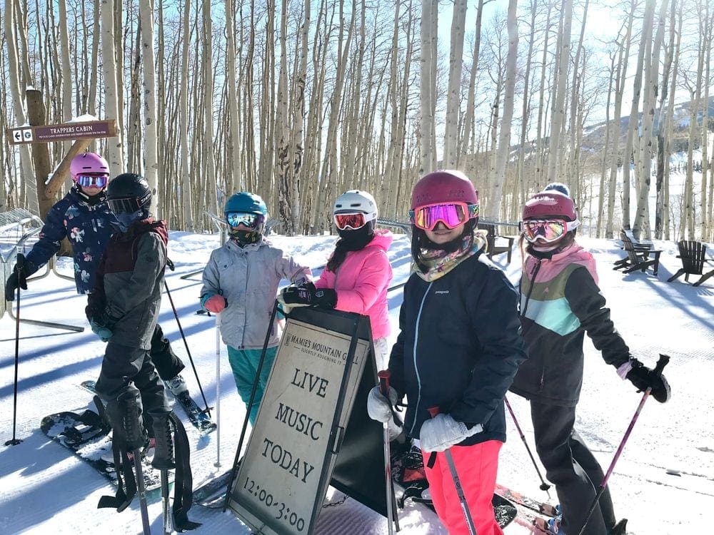 Six young kids in full snow gear, helmets, and goggles go skiing in Vail during the winter.