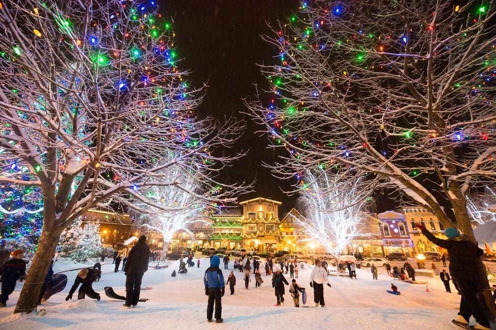 A crowd of people wanders through a large light display among trees and snow in Leavinworth, Washton.