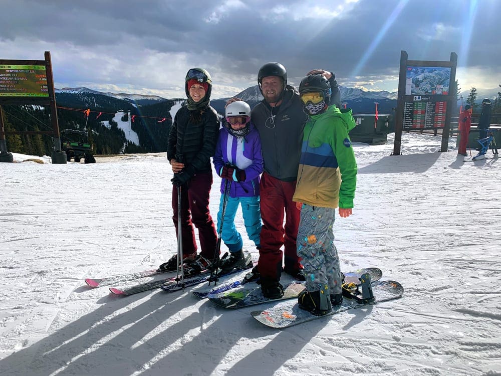 A family of four wearing snowgear stands on an assortment of skis and snowboards at Keystone, one of the best Colorado ski resorts for families.