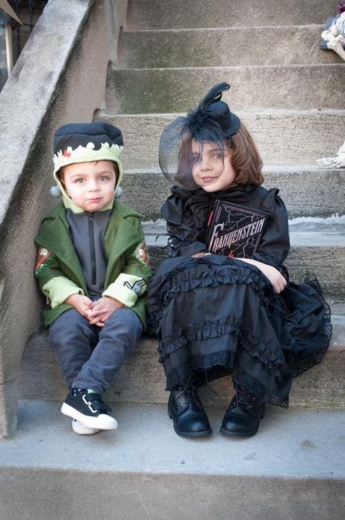 Two young kids sit on a stoop, one is dressed as Mary Shelley, while the other is Frankenstein’s Monster.