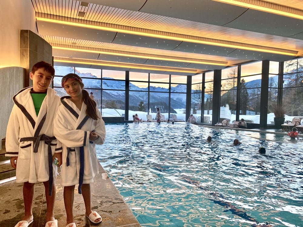 Two kids smile while wearing their Suvretta House robes, near the indoor pool.