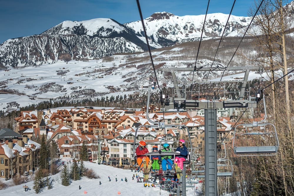 A family of four sits on a ski lift with an expansive view of Telluride behind them.