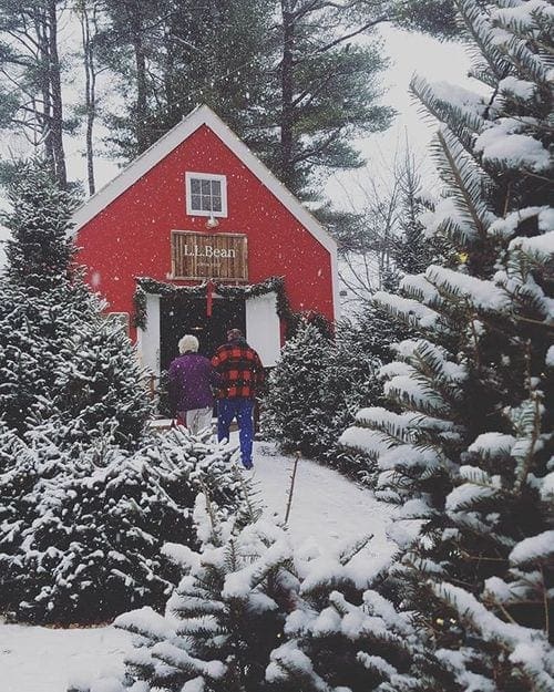 Two people walk toward a red barn covered in snow a the L.L. Bean headquarters in Freeport, Maine, one of the most magical Christmas towns for families.