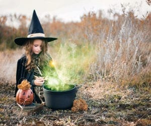 Little girl dressed in a witch costume and mixing potion.