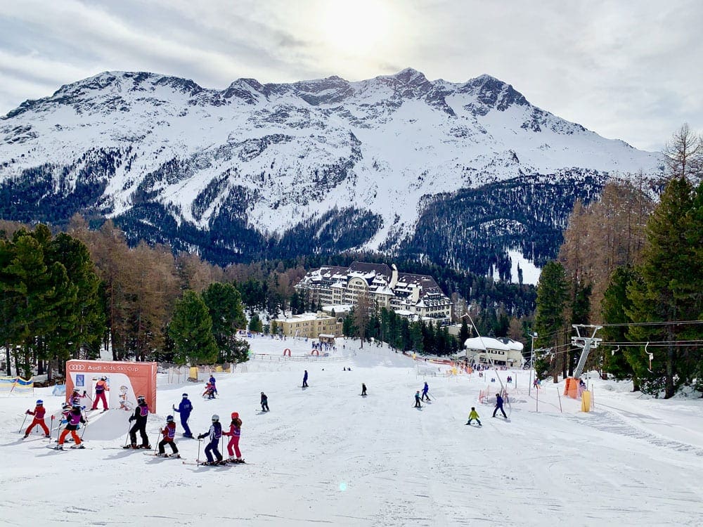 Suvretta House Ski School at St. Moritz, featuring a snowy mountain and several skiers in the distance.