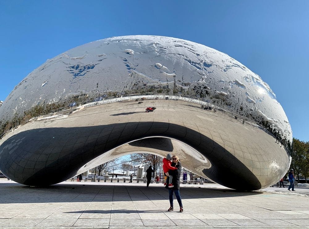 A mom holds her son in front of a snow-covered "Bean", one of the best kids activities in Chicago.