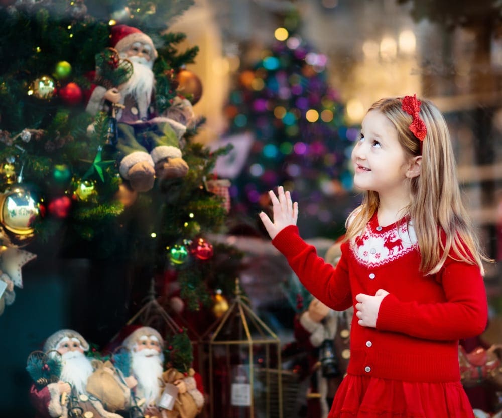 A young girl wearing a red dress looks up at a lovely Christmas tree.