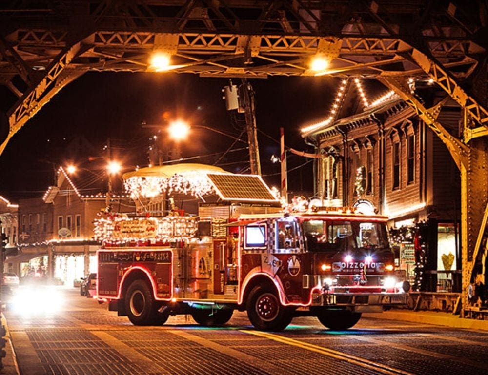 A fire truck lit up with Christmas lights drives down the street as part of a holiday parade in Mystic, Connecticut, one of the best Christmas towns in the Northeast.